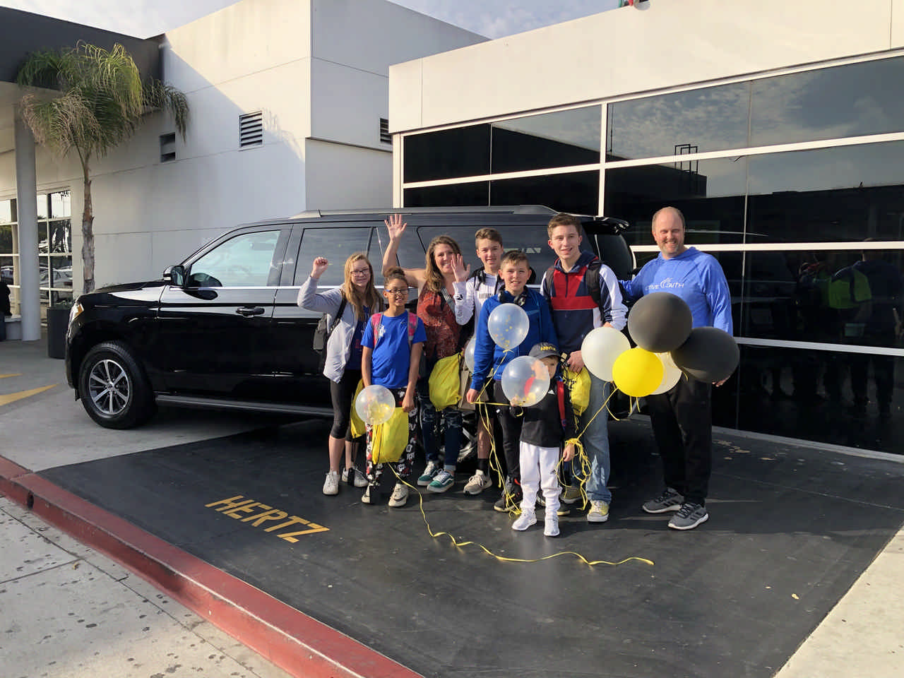 family standing beside rental Suburban with balloons on a JAJF WOW experience 
