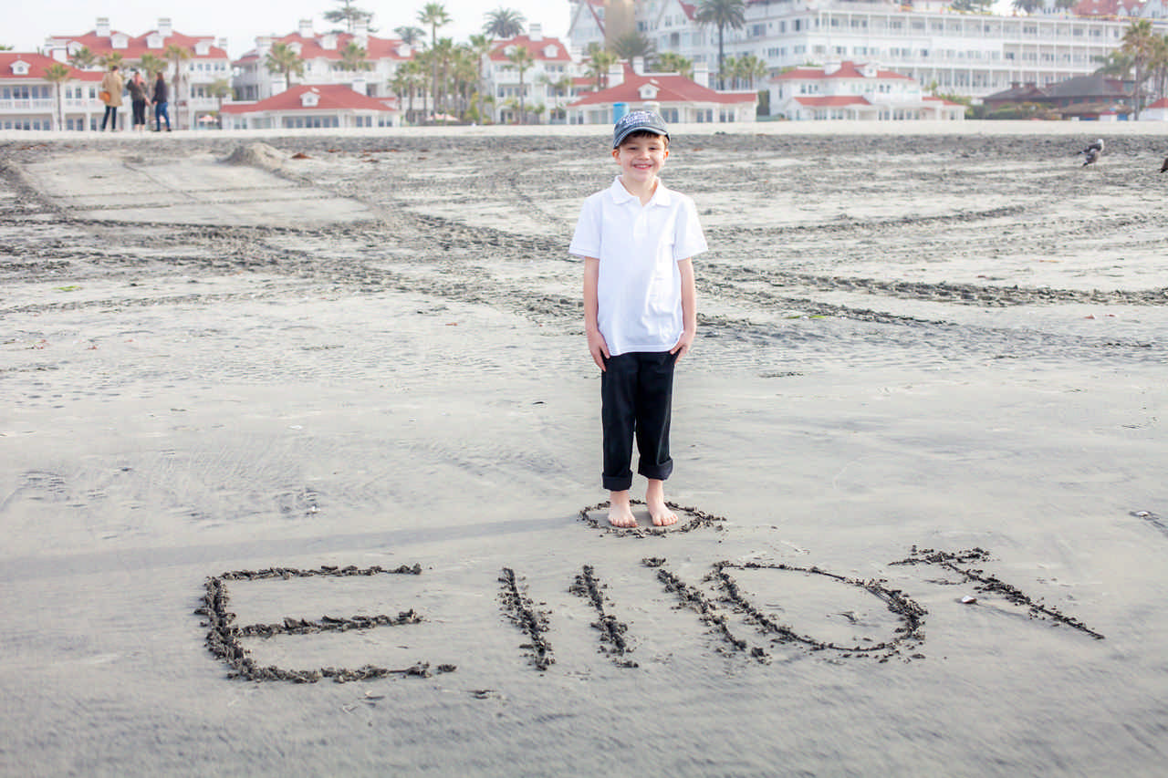 young boy posing by his name Elliot drawn in the sand 