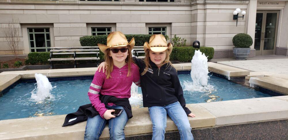 sisters in cowgirl hats sitting on fountain enjoying The Power of WOW experience 