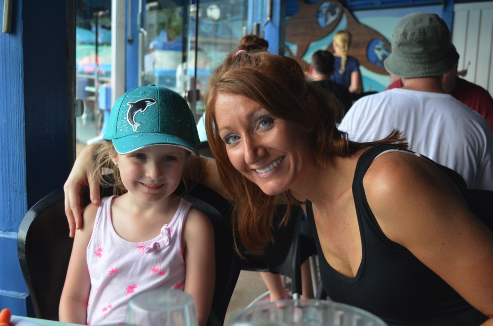 mom with arm around young daughter in blue hat at a restaurant during a JAJF trip treating the families not the cancer 