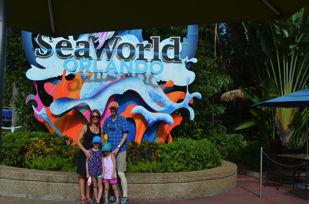 mom and dad with two young daughters in front of Sea World Orlando sign during a JAJF trip treating the families not the cancer 