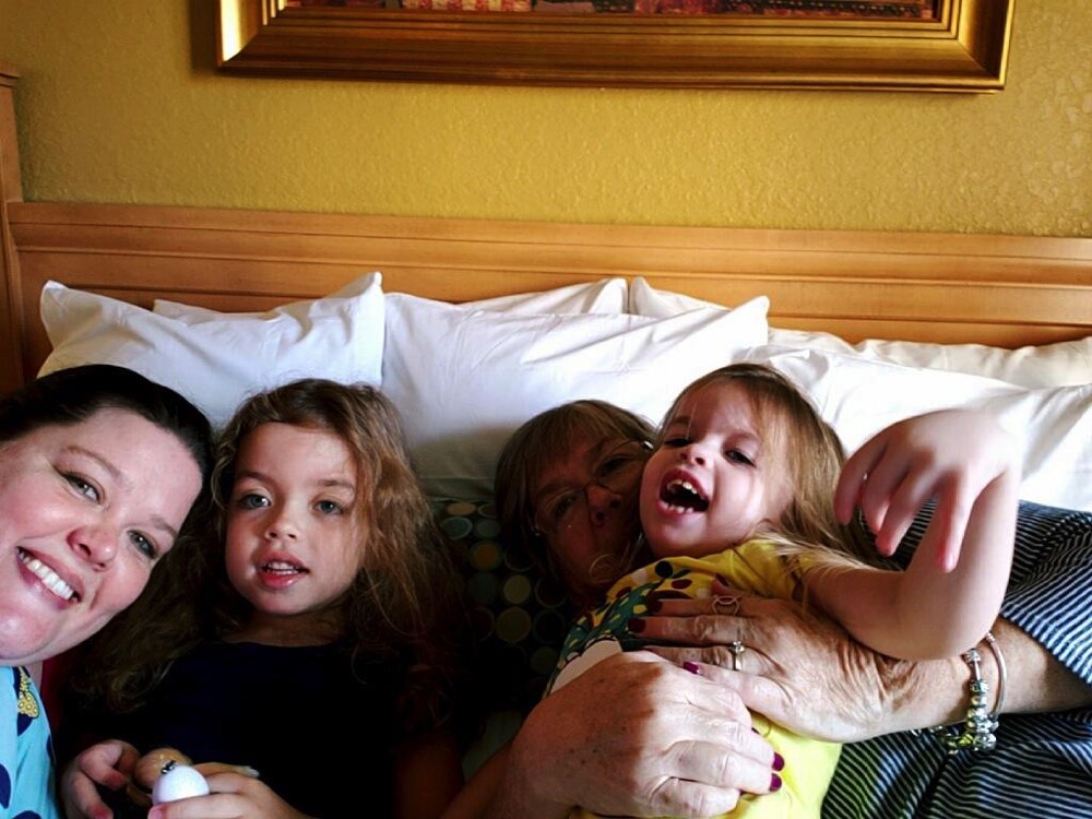 mom and dad with young daughters on hotel bed during a JAJF trip treating the families not the cancer 