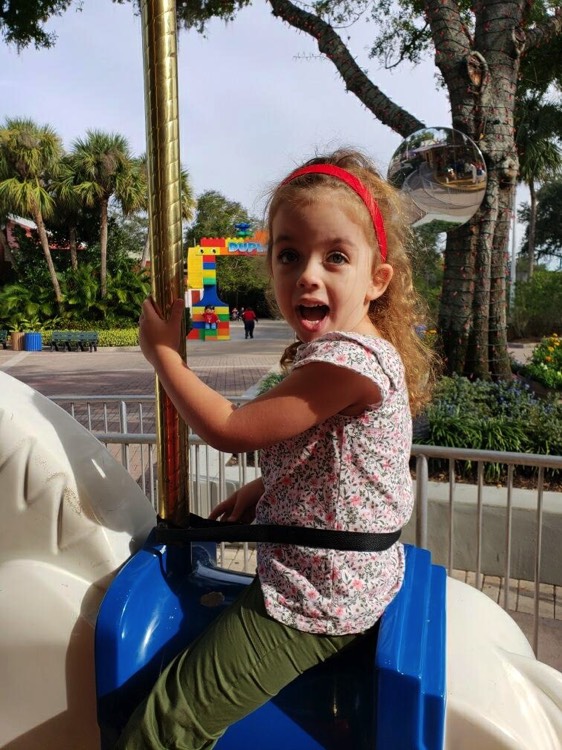 little girl with red headband on carousel during a JAJF trip treating the families not the cancer 